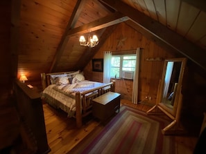 A cozy attic bedroom with a wooden bed, a bench, and a chandelier. - Beautiful Log Cabin For Romantic Getaways 20 Acres (Logan)