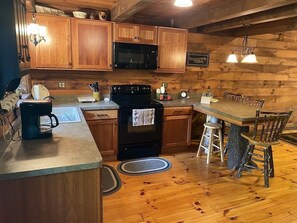 A wooden cabin-style kitchen with a central island, a stove, a microwave, and wooden cabinets. - Beautiful Log Cabin For Romantic Getaways 20 Acres (Logan)