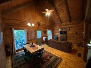 A cozy cabin interior with a dining area, sofa, and television. - Beautiful Log Cabin For Romantic Getaways 20 Acres (Logan)