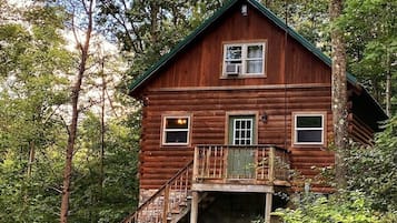 A wooden cabin with a balcony, surrounded by dense forest.