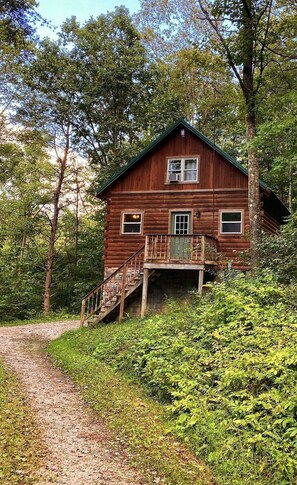 A wooden cabin with a balcony, surrounded by dense forest. - Beautiful Log Cabin For Romantic Getaways 20 Acres (Logan)