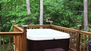 Un bain à remous sur une terrasse en bois, entouré d’une forêt dense.