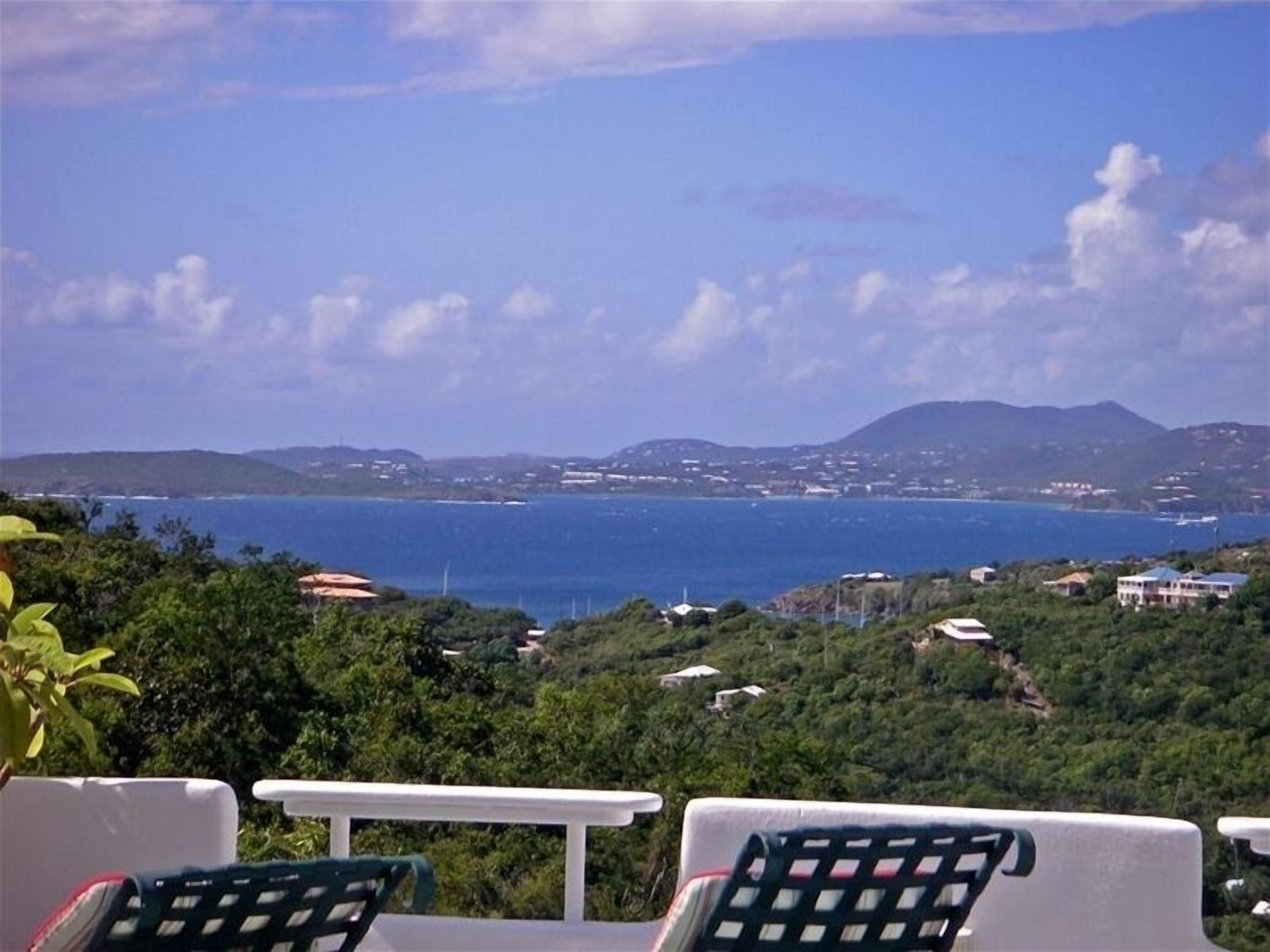 Terraço com duas cadeiras e vista para a costa, com casas e céu claro.