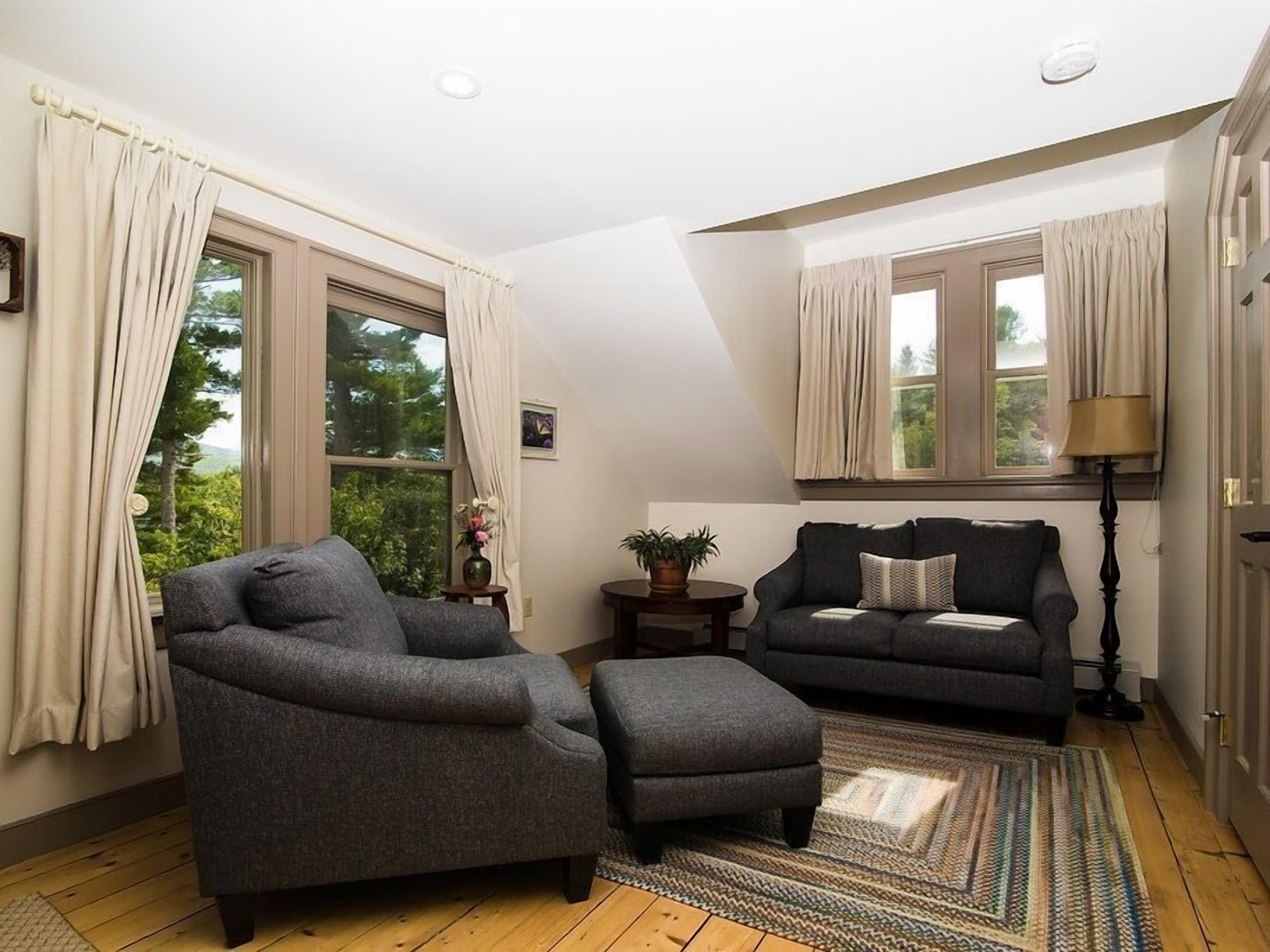 Un salon chaleureux avec un canapé gris, un pouf assorti et un tapis à motifs.