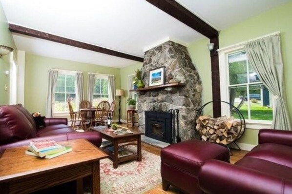 A cozy living room with a stone fireplace, leather sofas, and a dining area with a table and chairs. - Queen Room with Mtn Views (Keene)