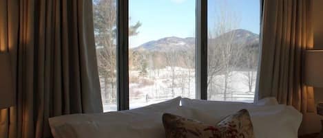 A hotel room with a bed, a window with curtains, and a view of mountains.