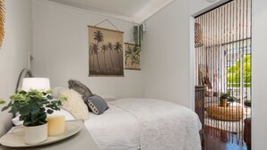 A bedroom with a bed, a bedside table with a plant and candle, and a view of the outdoors through a bamboo screen. - St Martini 416 (Cape Town)