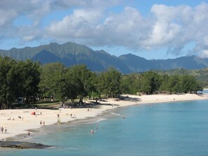 A beach with clear blue water, sandy shore, and mountains in the background.