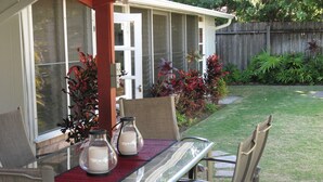 Eine Terrasse mit einem Glastisch und Stühlen, umgeben von einem Garten mit verschiedenen Pflanzen und einem Holzzaun.