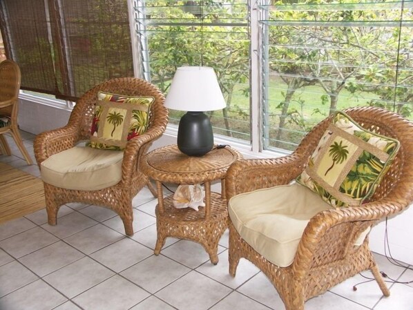 A room with wicker furniture, including two chairs and a small table with a lamp.