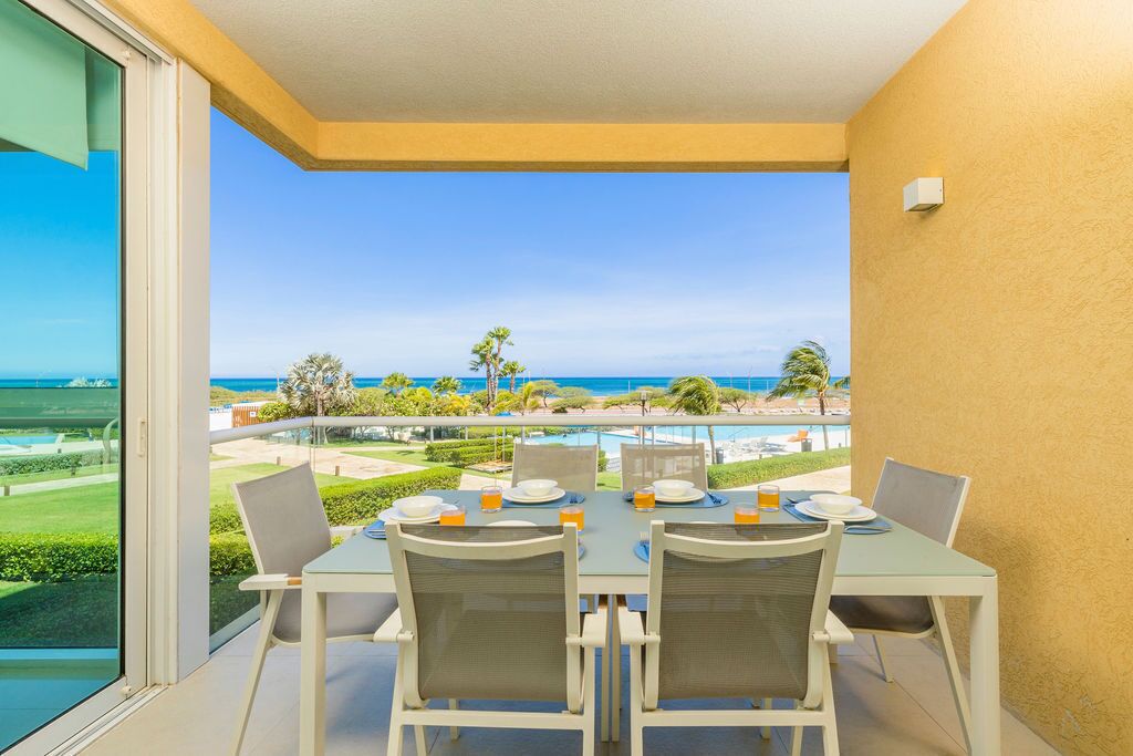 En balkon med et bord dækket til to, med udsigt over en pool og en anlagt have.