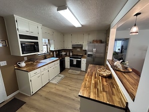 Una cocina moderna con armarios blancos, encimera de madera, refrigerador de acero inoxidable y microondas integrado.