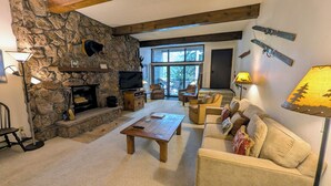 A living room with a stone fireplace, a television, a wooden coffee table, and a sofa. - Spacious Condo w/ FREE WiFi, Parking, Heated Pool, Hot Tubs, Ski Shuttles (Avon)