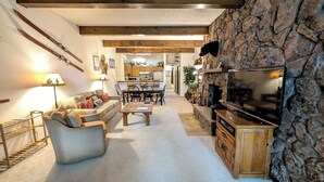 A cozy living room with a stone fireplace, a television, and a dining area with wooden furniture. - Spacious Condo w/ FREE WiFi, Parking, Heated Pool, Hot Tubs, Ski Shuttles (Avon)