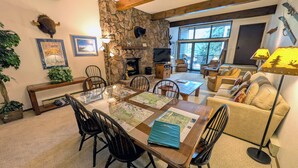 A cozy living room with a stone fireplace, a dining table with maps, and a comfortable seating area. - Spacious Condo w/ FREE WiFi, Parking, Heated Pool, Hot Tubs, Ski Shuttles (Avon)