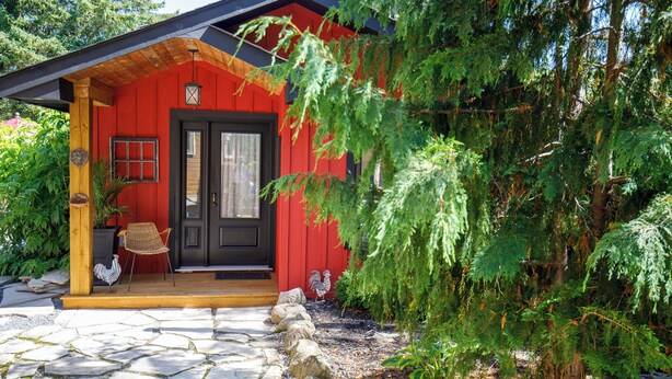 A red building with a black door, a wooden porch, and a stone pathway leading to the entrance. - Runaway Rooster B&B -- Guest Cottage
 (Prince Edward)