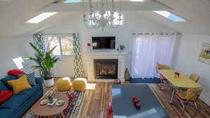 A living room with a sofa, coffee table, fireplace, TV, and dining area. - Runaway Rooster B&B -- Guest Cottage
 (Prince Edward)