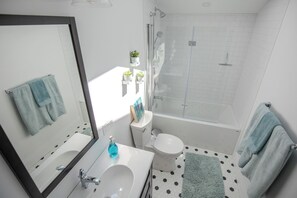 A modern bathroom with a white sink, toilet, and shower. There are two towels hanging on the wall and a small potted plant on the shelf. - Runaway Rooster B&B -- Guest Cottage
 (Prince Edward)