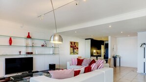 A modern living room with a white sofa, a flat-screen TV, and a glass shelf with decorative items. - Dunmore Place (Cape Town)