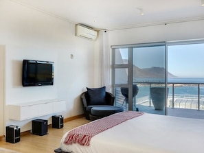 A modern bedroom with a large bed, a TV, speakers, and a view of the sea. - Dunmore Place (Cape Town)