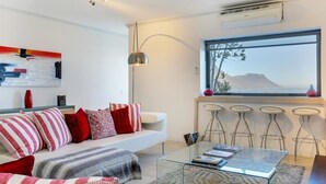 A modern living room with a sofa, a glass coffee table, and a view of a mountain through a large window. - Dunmore Place (Cape Town)