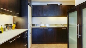 A modern kitchen with dark wood cabinets, a stainless steel refrigerator, and a glass-fronted cabinet. - Dunmore Place (Cape Town)