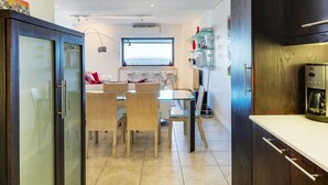 A modern kitchen with a dining area, featuring a coffee machine, cabinets, and a window with a view. - Dunmore Place (Cape Town)