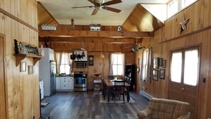 Un interior de cabaña acogedor con paredes de madera, una zona de comedor, una cocina con electrodomésticos modernos y un ventilador de techo.