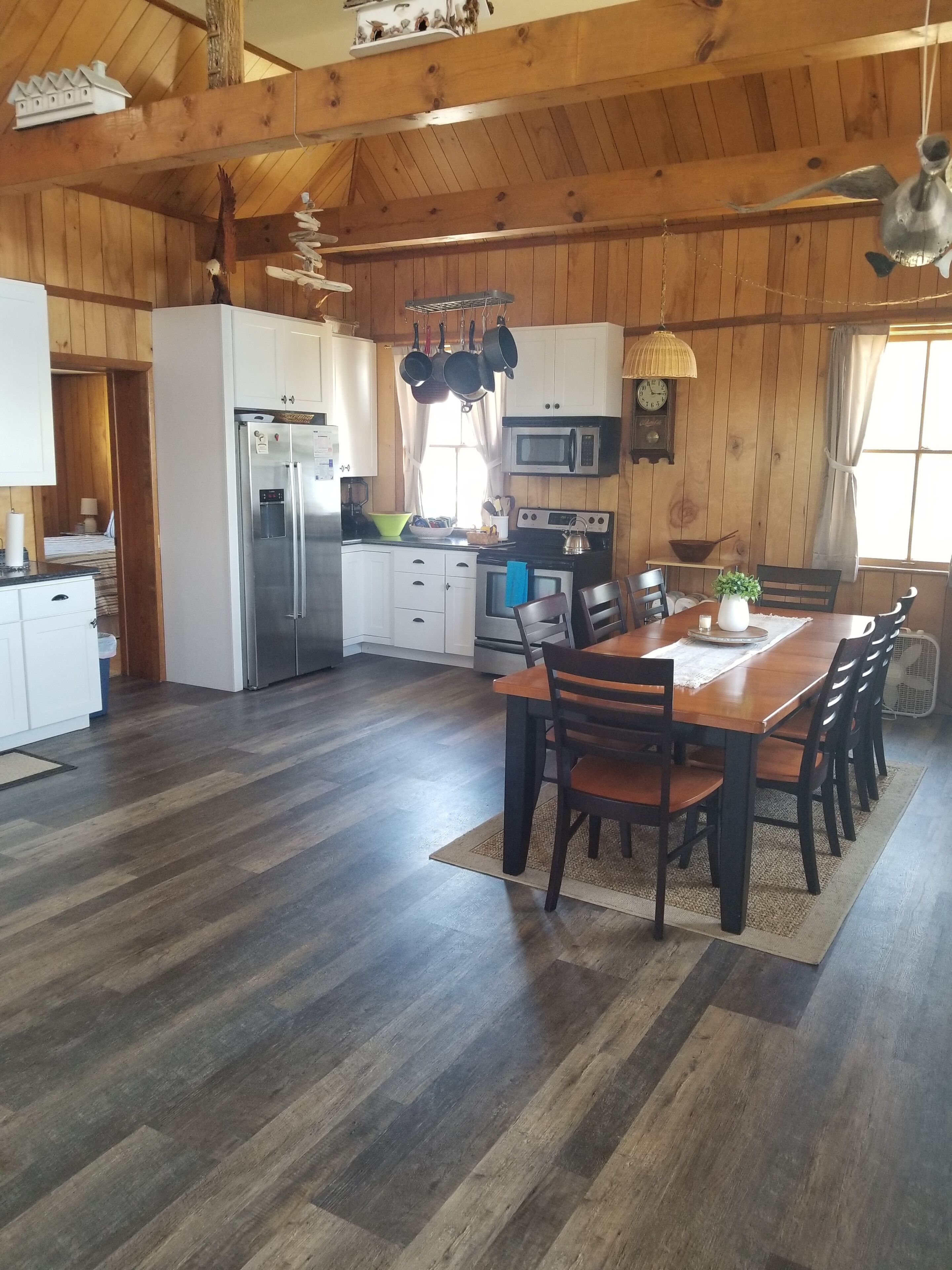 Une cuisine spacieuse avec un plancher en bois, un coin repas avec une table et des chaises en bois, et une grande fenêtre qui laisse entrer la lumière naturelle.
