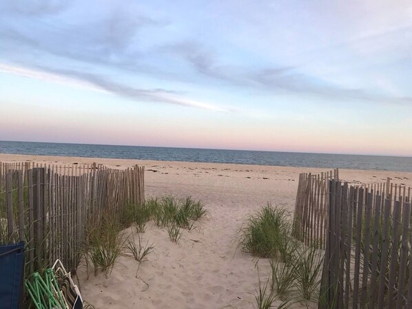 Walk along the beach pathway to the shoreline, bordered by lush vegetation and a wooden fence.