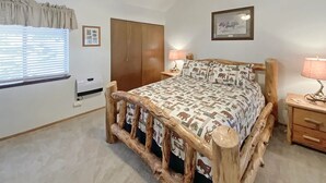 A bedroom with a rustic wooden bed frame, a ceiling fan, a window with blinds, a wardrobe, and a bedside table with a lamp. - Angel Fire Chalet park and walk (Angel Fire)