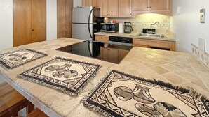 A kitchen with wooden cabinets, a refrigerator, a microwave, a coffee maker, and a large island with a black countertop. - Angel Fire Chalet park and walk (Angel Fire)