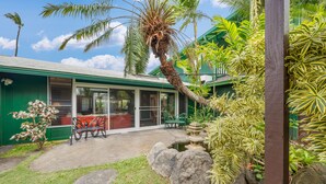A house with a green exterior, a patio with a table and chairs, and a small rock garden.