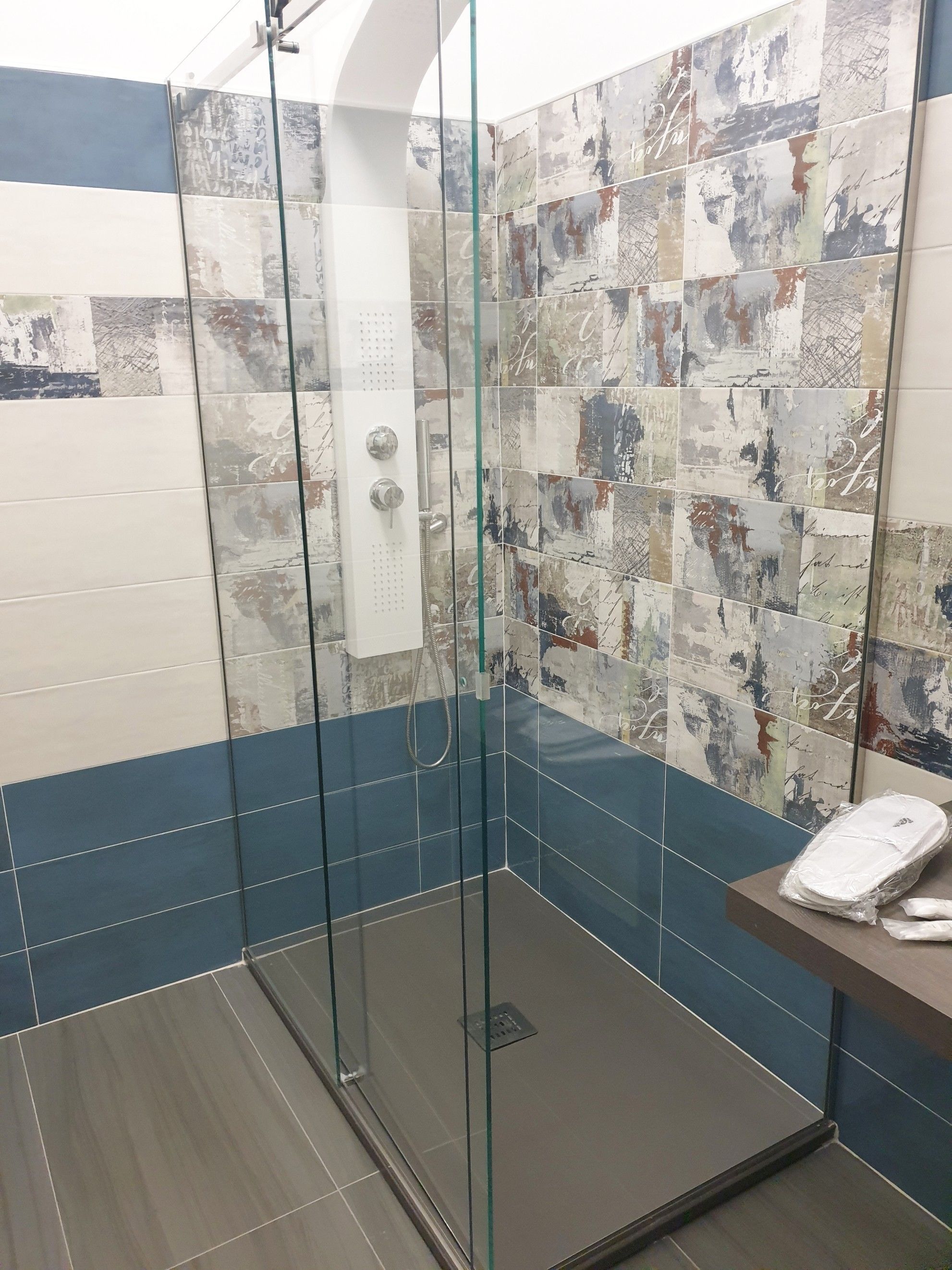 Une douche avec des portes en verre, un lavabo blanc et un mur recouvert de carreaux aux motifs abstraits.