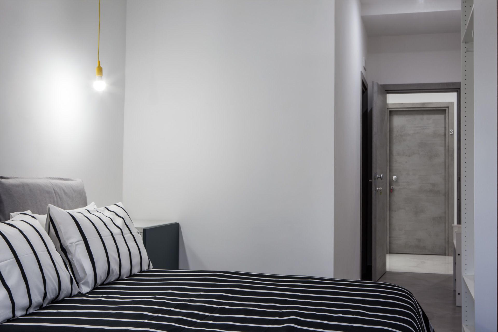 A bedroom with a bed, pillows, a bedside table, and a door leading to another room.