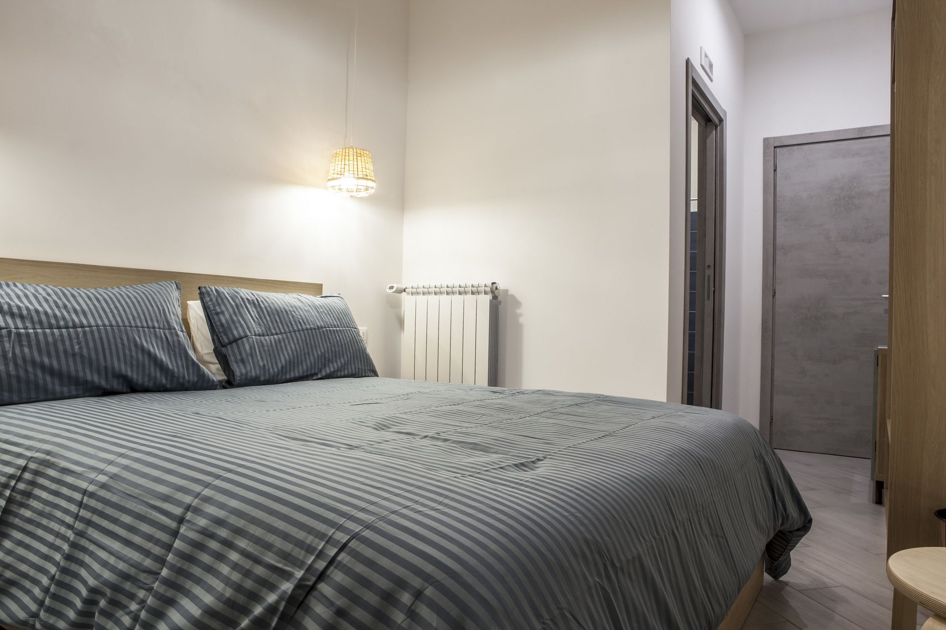 A modern bedroom with a large bed, a bedside table, a radiator, and a door.