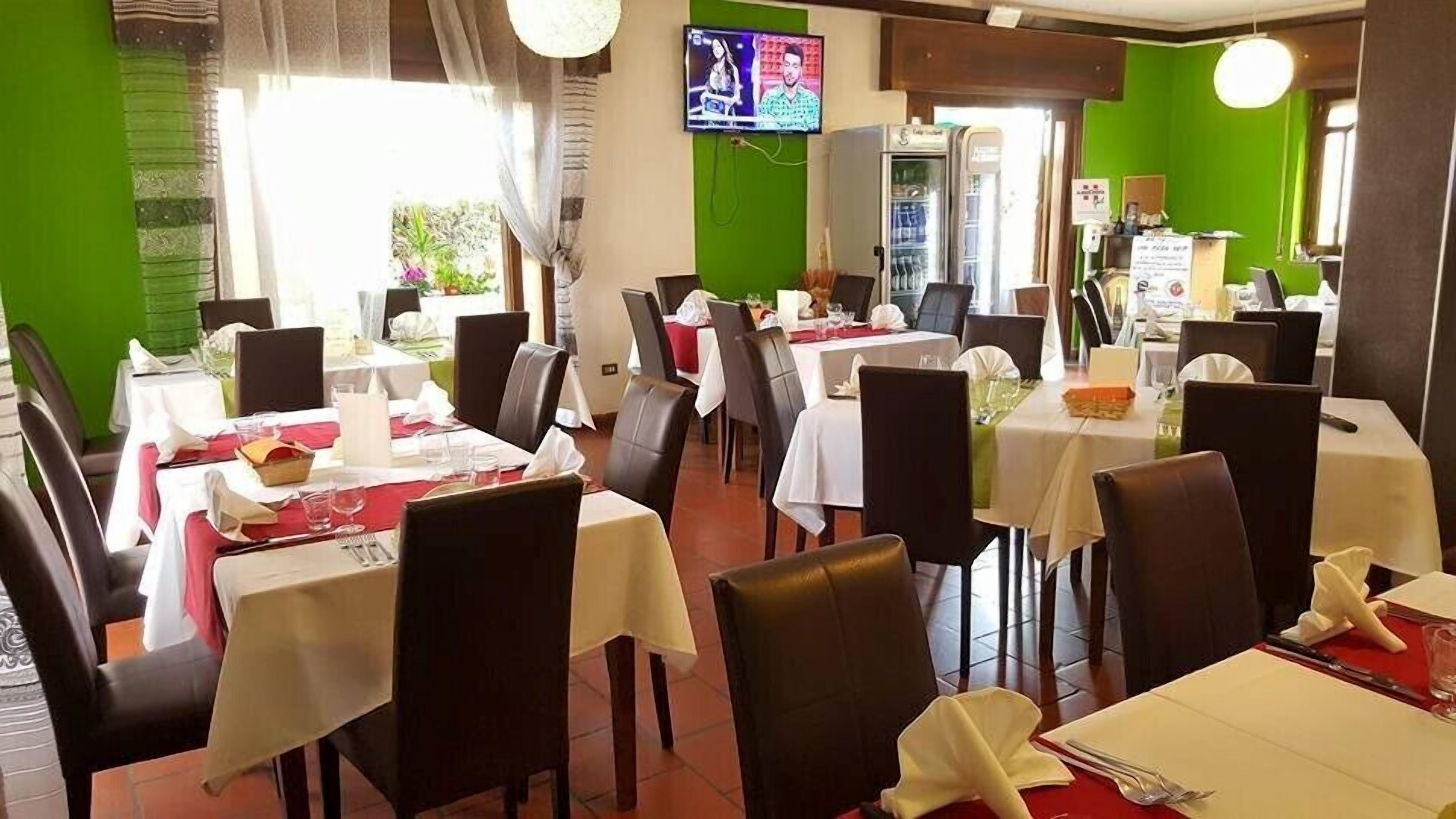 A restaurant with multiple tables set for dining, a television screen mounted on the wall, and a green accent wall.
