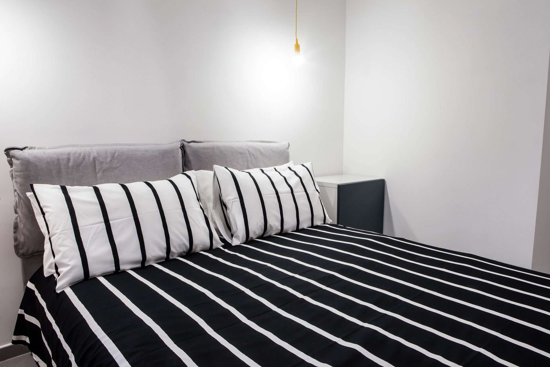 A bed with black and white striped bedding, a gray headboard, and a bedside table with a lamp.