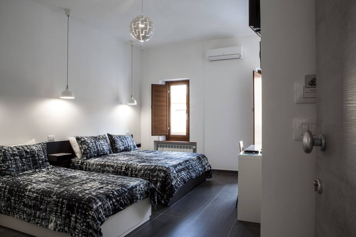 Une chambre moderne avec deux lits, un luminaire suspendu et une fenêtre donnant sur un beau paysage.