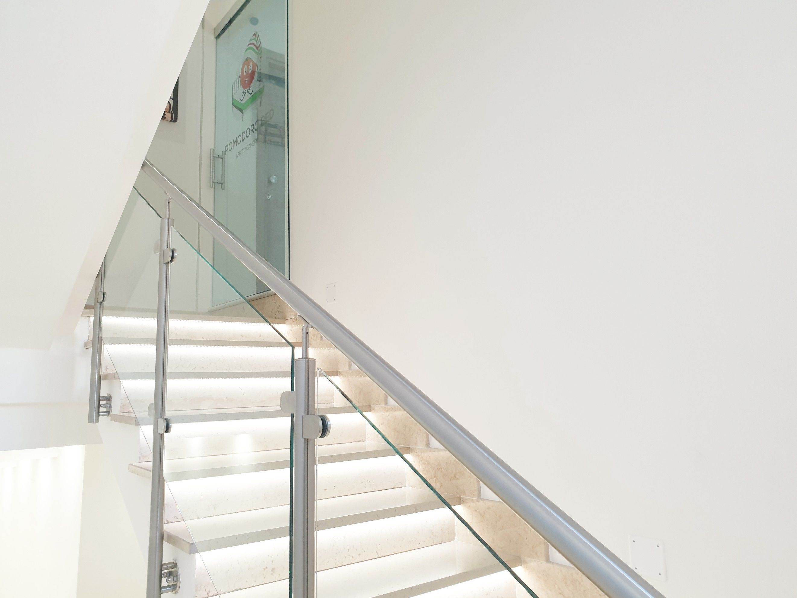 A modern staircase with glass railings and a white wall.