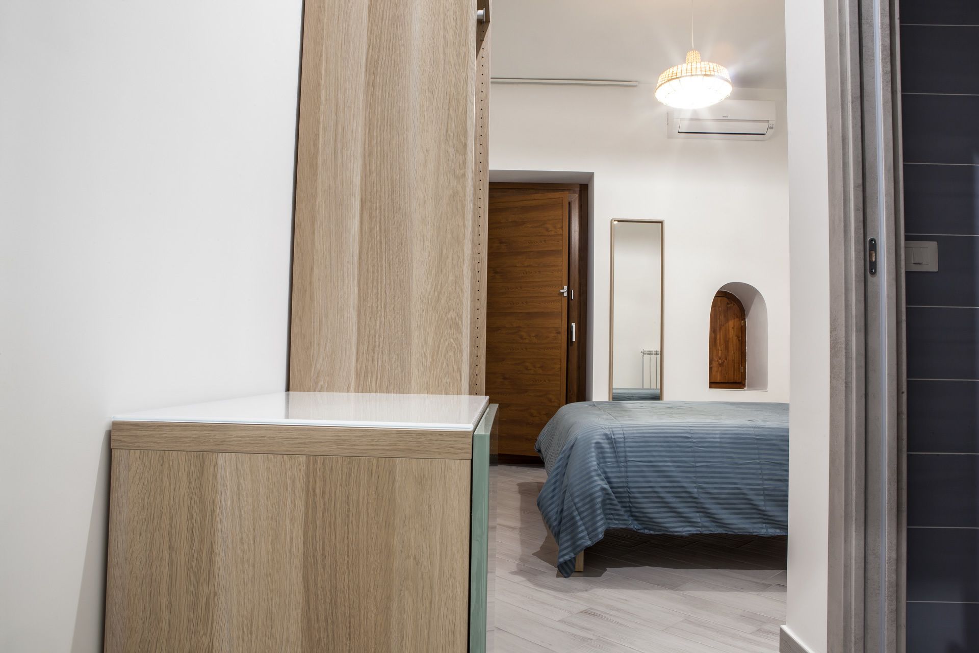 Ein Schlafzimmer mit einem Holzschrank, einem Bett mit gestreifter Bettdecke, einer Holztür und einer Deckenleuchte.
