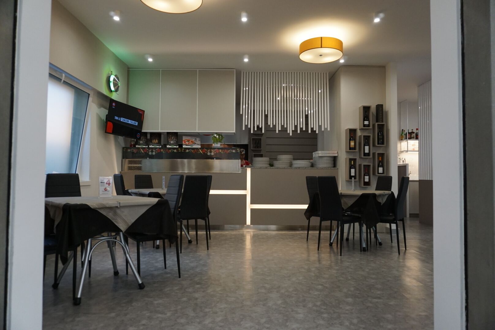 A modern restaurant with a bar area, dining tables, and a kitchen in the background.