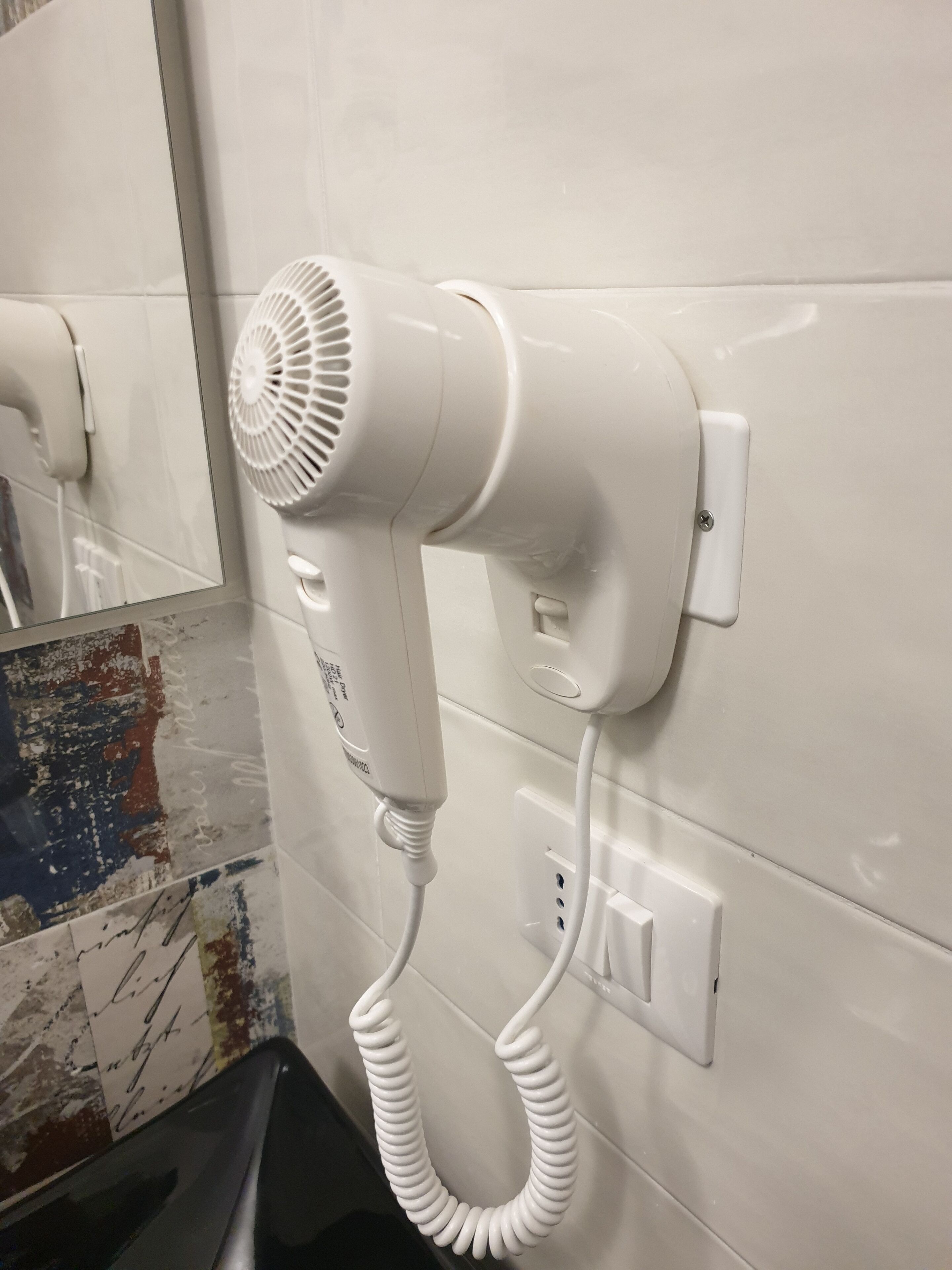 Un sèche-cheveux blanc fixé au mur, avec une prise de courant et un interrupteur.