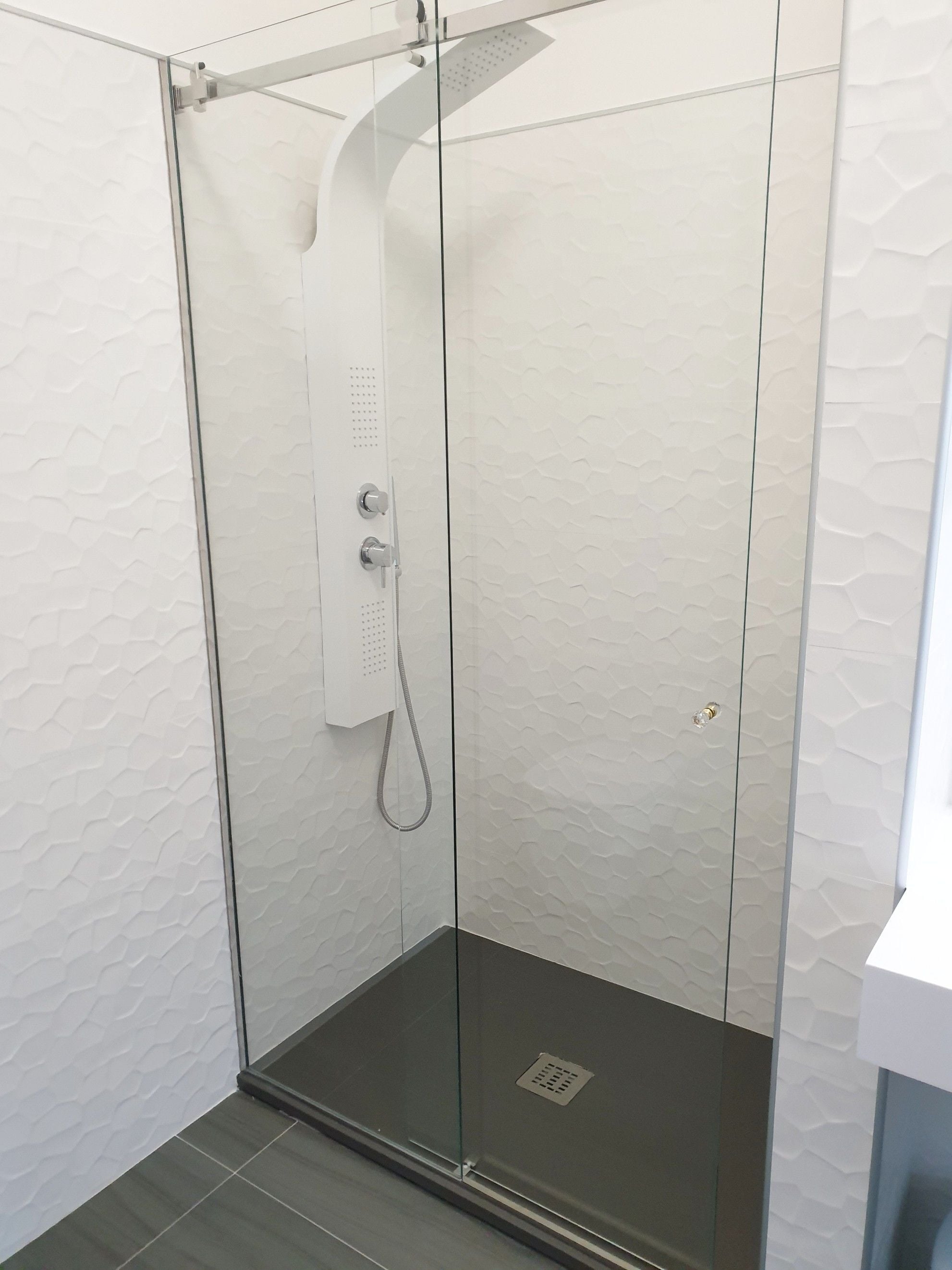 A glass-enclosed shower with a handheld showerhead and a control panel.