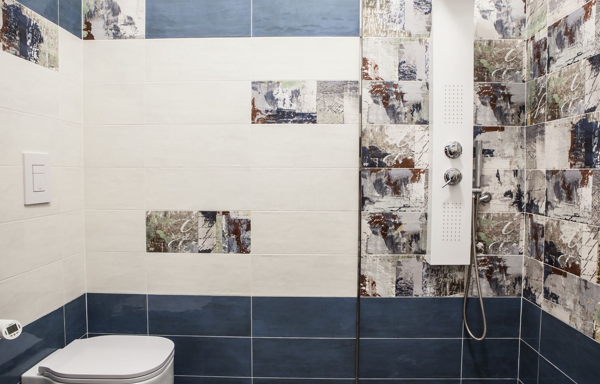 A bathroom with a white toilet, a shower with a handheld showerhead, and a wall with a mix of white and blue tiles.