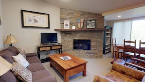 A living room with a stone fireplace, a television, a sofa, and a coffee table. - Terracehouse 55 - Ski by Day, Soak by Night | Steps to Slopes & Hot Tub (Snowmass Village)