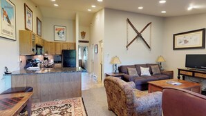 A spacious living area with a sofa, coffee table, and a television. A kitchen with wooden cabinets and a microwave is visible in the background. - Terracehouse 55 - Ski by Day, Soak by Night | Steps to Slopes & Hot Tub (Snowmass Village)