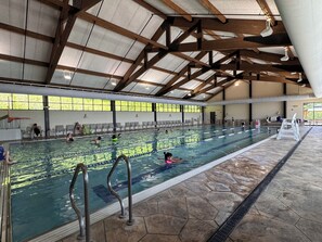 Una piscina al coperto con diverse corsie, una sedia per il bagnino e un pavimento piastrellato.