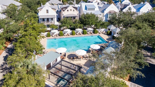 Een resort met een zwembad, omringd door ligbedden en parasols, met op de achtergrond huizen en bomen.