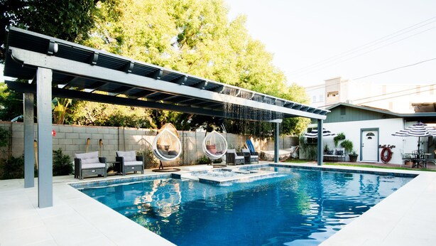 Una piscina con pérgola, sillas de descanso y una zona de estar cubierta.